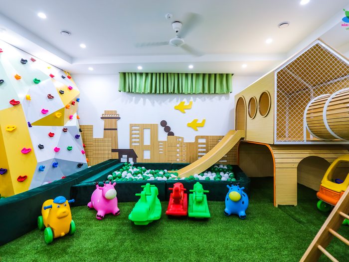 Khu vui chơi của trường có tường leo, nhà gỗ, cầu trượt và thảm cỏ