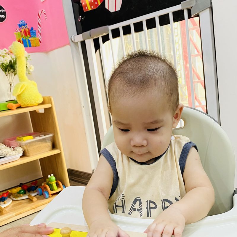 Bé lớp Baby ngồi ghế ăn, chăm chú nhìn xuống bàn học